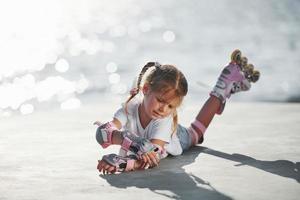 Lying down. Cute little girl with roller skates outdoors near the lake at background photo