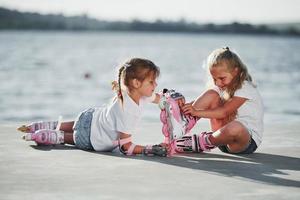 Two little girls with roller skates outdoors near the lake at background photo