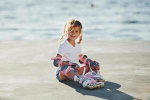 Girl in roller skates sits on the beach near the lake at daytime photo