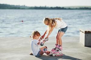 Two kids learning how to ride on roller skates at daytime near the lake photo