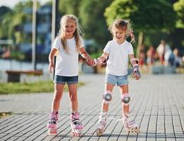 Two cute kids riding by roller skates in the park at daytime photo