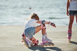 Two kids learning how to ride on roller skates at daytime near the lake photo