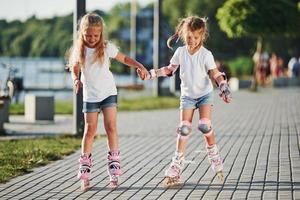 Two cute kids riding by roller skates in the park at daytime photo