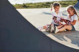 Relaxing and have conversation. On the ramp for extreme sports. Two little girls with roller skates outdoors have fun photo