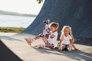 Trying new skate. Two cute female kids have fun outdoors in the park photo
