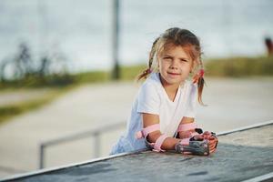 Cute little girl with roller skates outdoors sits on the ramp for extreme sports photo