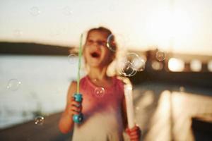 increíble luz del sol. niña feliz jugando con burbujas cerca del lago en el parque