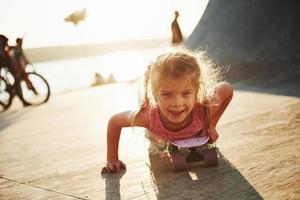 First attempts. Sunny day. Kid have fun with skate at the ramp. Cheerful little girl photo