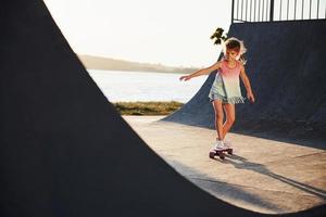 Sunny day. Kid have fun with skate at the ramp. Cheerful little girl photo