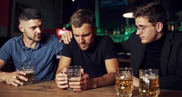 Three male friends in the bar. Supporting sad friend. Unity of people. With beer on the table photo