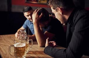 Three male friends in the bar. Supporting sad friend. Unity of people. With beer on the table photo