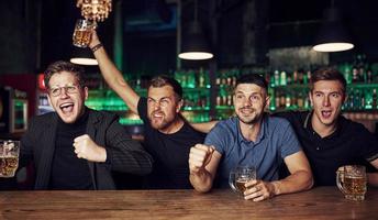 es una meta celebrando la victoria. tres aficionados al deporte en un bar viendo fútbol. con cerveza en las manos foto