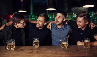 Three friends resting in the pub with beer in hands. Having conversation photo