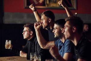 tres aficionados al deporte en un bar viendo fútbol. con cerveza en las manos foto