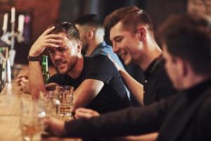 vista lateral. amigos descansando en el pub con cerveza en las manos. teniendo una conversación foto
