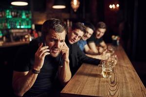 el hombre habla por teléfono. tres aficionados al deporte en un bar viendo fútbol. con cerveza en las manos