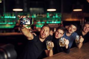 haciendo una autofoto. tres amigos descansando en el pub con cerveza en las manos. teniendo una conversación foto