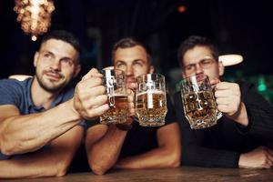 Knocking glasses. Three sports fans in a bar watching soccer. With beer in hands photo