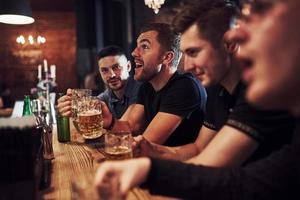 gente positiva amigos descansando en el pub con cerveza en las manos. teniendo una conversación foto