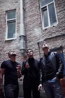 Smoking together. Three male friends stands outside the bar. Having conversation. In nice clothes photo