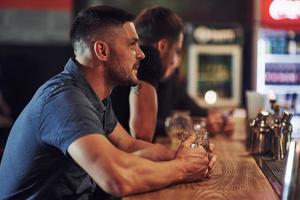 Side view. Friends resting in the pub with beer in hands. Having conversation photo