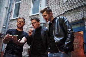 Three male friends stands outside the bar and smoking. Having conversation. In nice clothes photo