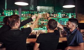 muchas de botellas con alcohol en los estantes. amigos descansando en el pub con cerveza en las manos. teniendo una conversación foto