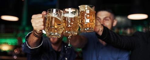 golpeando vasos. tres aficionados al deporte en un bar viendo fútbol. con cerveza en las manos foto