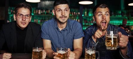 emociones sinceras. tres aficionados al deporte en un bar viendo fútbol. con cerveza en las manos foto