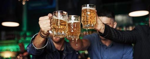 golpeando vasos. tres aficionados al deporte en un bar viendo fútbol. con cerveza en las manos foto