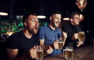 Three sports fans in a bar watching soccer. With beer in hands photo