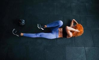 Top view. Sporty redhead girl have fitness day in gym at daytime. Muscular body type photo