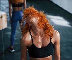 Sporty redhead girl have fitness day in gym at daytime. Muscular body type photo