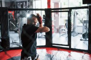 Young boxer in red bandages have exercise. In the gym on the cage photo