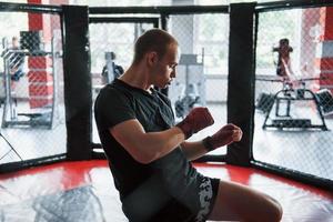 Young boxer in red bandages have exercise. In the gym on the cage photo