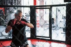 el boxeador joven con vendas rojas tiene ejercicio. en el gimnasio en la jaula foto