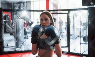 Beautiful female boxer in blue gloves have exercise. In the gym on the cage photo