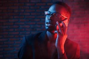 Having conversation by using phone. Futuristic neon lighting. Young african american man in the studio photo