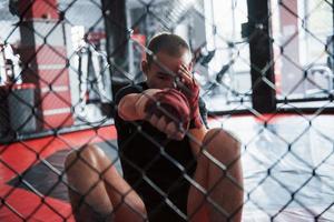 desde la posición hacia abajo. el boxeador joven con vendas rojas tiene ejercicio. en el gimnasio en la jaula foto