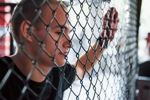 Side view. Taking a break. Sportsman at boxing ring have exercise. Leaning on the fence photo