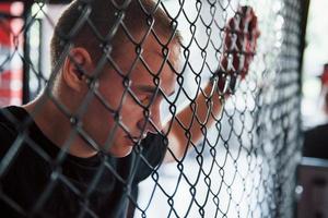 Side view. Taking a break. Sportsman at boxing ring have exercise. Leaning on the fence photo