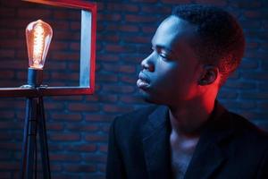 Looks at bulb. Futuristic neon lighting. Young african american man in the studio photo