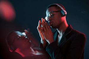 disfrutando escuchando música en auriculares. en vasos iluminación de neón futurista. joven afroamericano en el estudio foto