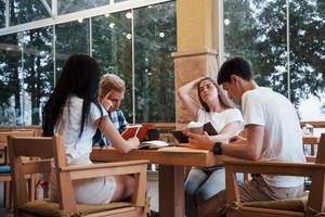 Sitting in cafe and having conversation. Four young students in casual clothes have meeting at rainy day photo