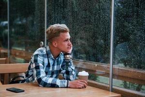 retrato de un joven estudiante que se sienta en un café en un día lluvioso. una persona foto