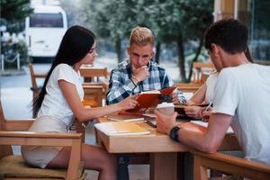 Sitting in cafe and having conversation. Four young students in casual clothes have meeting at rainy day photo