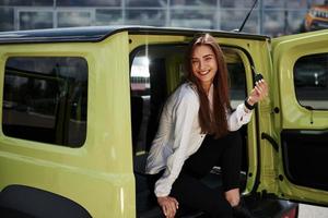 Young woman in white official clothes sits in green automobile outdoors photo