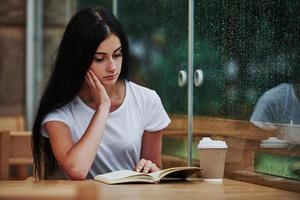 Portrait of young female student that sits in cafe at rainy day. One person only photo