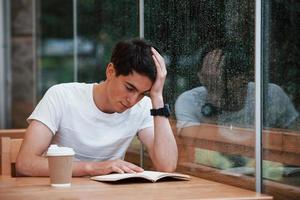 Portrait of young student that sits in cafe at rainy day. One person photo