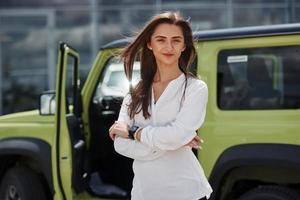 Young woman in white official clothes stands in front of green automobile outdoors photo